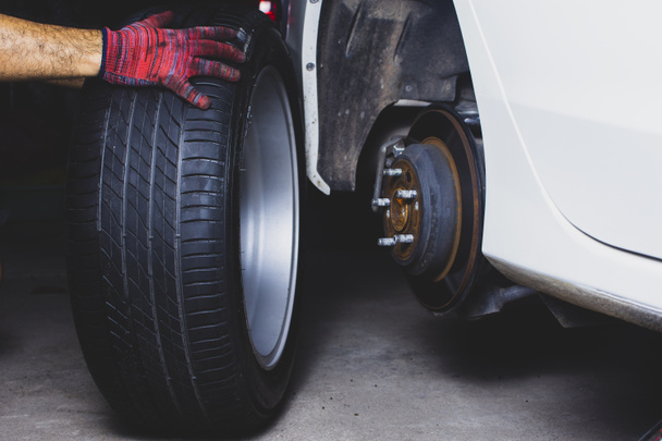 La mano del mecánico sostiene la rueda de aleación para cambiar la rueda de aleación en el cubo de la rueda en el taller de neumáticos del coche
. - Foto, imagen