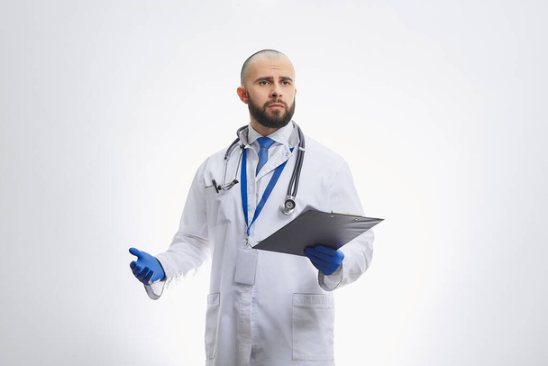 Un medico con uno stetoscopio e un blocco appunti con guanti medici usa e getta. Un medico calvo con la barba che si prepara ad esaminare i pazienti
. - Foto, immagini