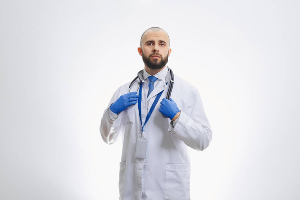 Een arts met een stethoscoop en wegwerphandschoenen. Een kale arts met een baard bereidt zich voor om patiënten te onderzoeken. - Foto, afbeelding