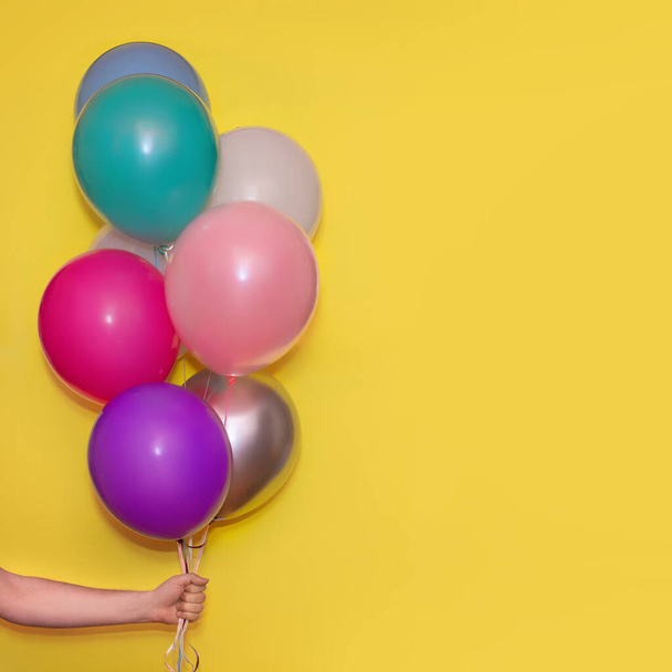 Hand holding colorful helium balloons isolated on yellow background!Holiday concept.Copy space for text. - Fotó, kép