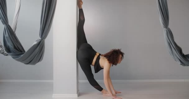 Atrakcyjna kubińska młoda kobieta stoi na sznurku przy ścianie w studiu jogi muchowej w zwolnionym tempie, elastyczna kobieta wykonuje ćwiczenia akrobatyczne i plastyczne, jogę i rozciąganie, 4k DCI 60p Prores 422 - Materiał filmowy, wideo