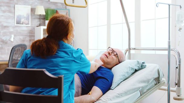 Un anciano enfermo en una cama de hospital recibe un chequeo del latido
 - Foto, Imagen