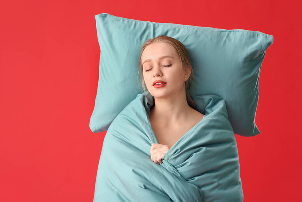 Schläfrige junge Frau mit Kissen und Decke auf farbigem Hintergrund - Foto, Bild