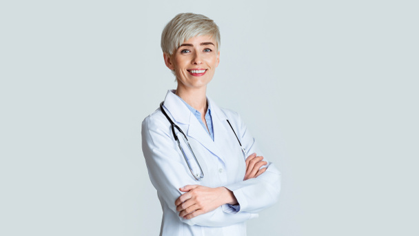 Портрет улыбающейся молодой женщины-врача в белом халате со стетоскопом, изолированный на светлом фоне
 - Фото, изображение
