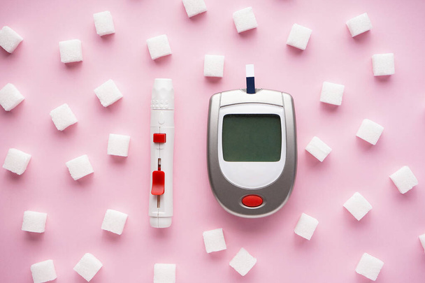 Digital glucometer, lancet pen and sugar cubes on a pink background, flat lay. Close-up. Diabetes concept. - Photo, Image