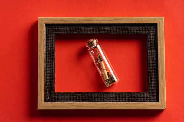 Miniature eiffel tower in bottle and empty frame against red background - Photo, Image