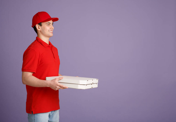 Υπηρεσίες ταχυμεταφορών. Νεαρός κούριερ με κόκκινη στολή παραδίδει πίτσα στο σπίτι - Φωτογραφία, εικόνα