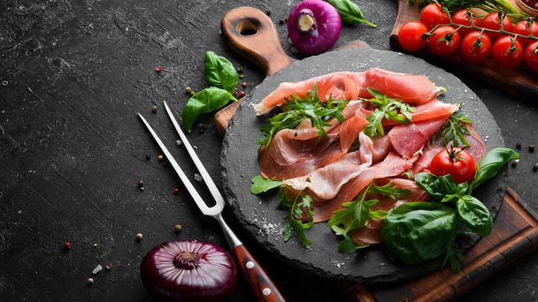 Prosciutto with arugula and basil on a black plate. Spanish cuisine. Top view. Free space for your text. - Photo, image