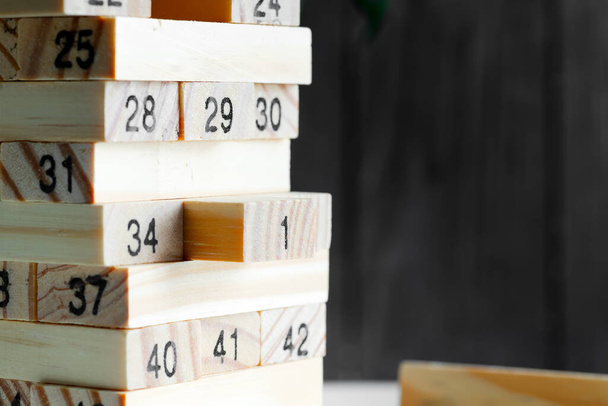 Kreativer Holzkonstrukteur aus Blöcken mit Zahlen vor schwarzem Hintergrund. Jenga-Spiel für Verdienst, Entwicklung und Bildung. - Foto, Bild