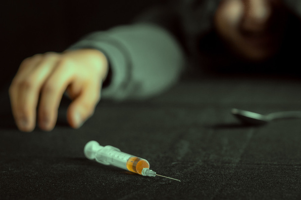 Grunge image of a depressed drug addict looking at a syringe and drugs - Fotó, kép