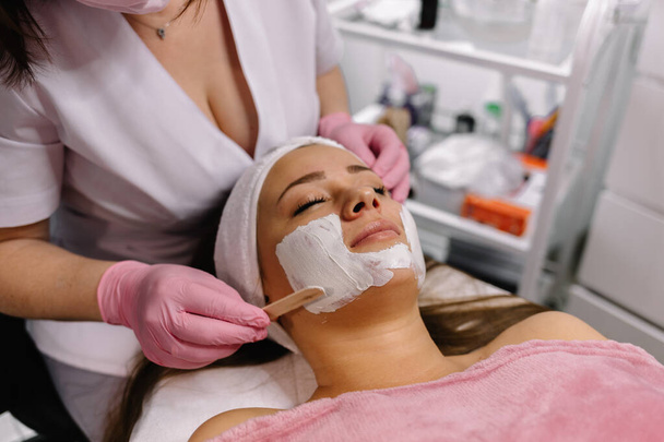 esteticista aplicando mascarilla facial a la joven, vista desde la parte superior
 - Foto, Imagen