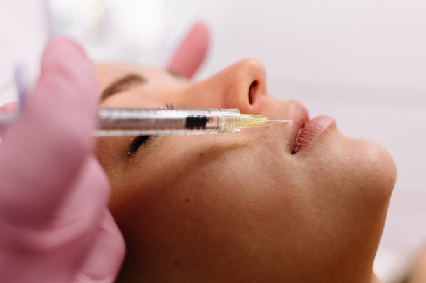Injection in patient woman lips to volume and correction shape making by doctor cosmetologist. Beautician injects filler collagen or hyaluronic acid into lips with syringe. Contour Plastic of Lips. - Foto, Bild