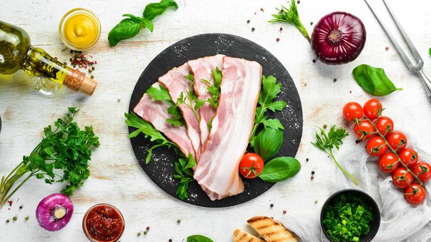 Slices of bacon with arugula and parsley on a black plate. Top view. Free space for your text. - Photo, Image