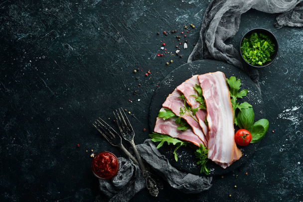Slices of bacon with arugula and parsley on a black plate. Top view. Free space for your text. - Фото, изображение