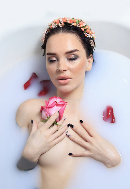 Beauty portrait of pretty young naked woman takes a bath with milk and roses petals and closed eyes - Zdjęcie, obraz