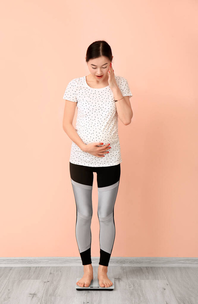 Mujer embarazada joven midiendo su peso contra la pared de color
 - Foto, imagen