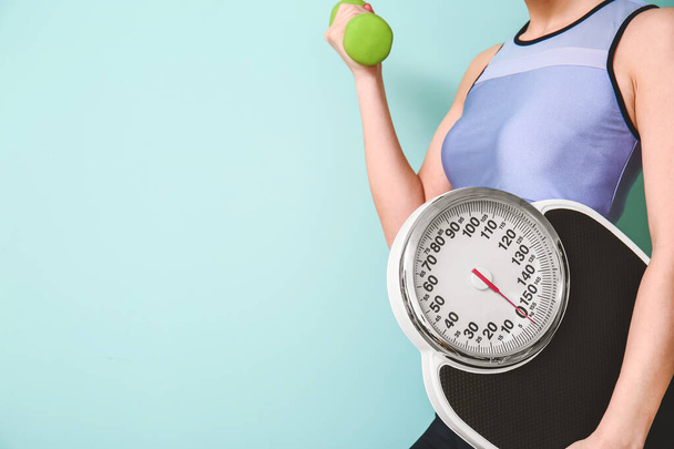 Young woman with weight scales and dumbbell on color background - Photo, Image