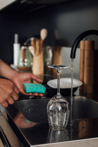 selective focus of wet glass near man holding sponge in kitchen  - Valokuva, kuva
