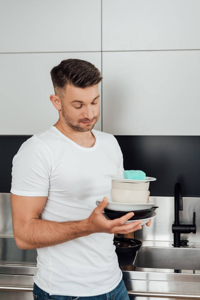 displeased man holding dirty plates in kitchen  - Valokuva, kuva