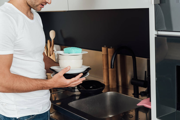 cropped view of man holding dirty plates and sponge in kitchen  - Foto, afbeelding