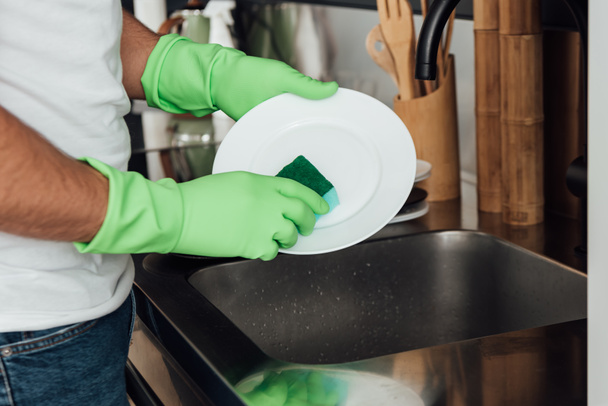 cropped view of man in rubber gloves washing plate with sponge  - Foto, Imagen