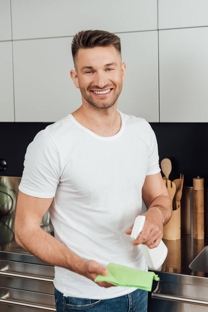 happy man holding rag and spray bottle while cleaning apartment  - Photo, Image