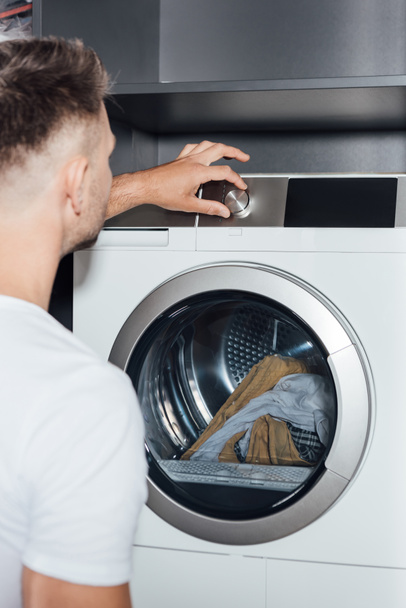 enfoque selectivo del botón de contacto del hombre en la lavadora moderna con ropa sucia
  - Foto, imagen