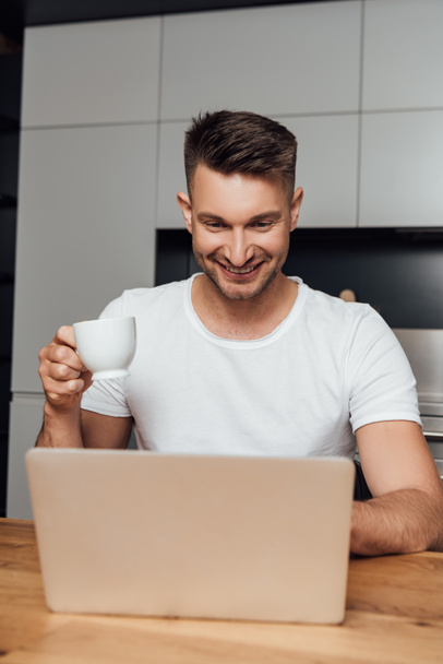 cheerful freelancer holding cup of coffee and looking at laptop  - Foto, Imagem