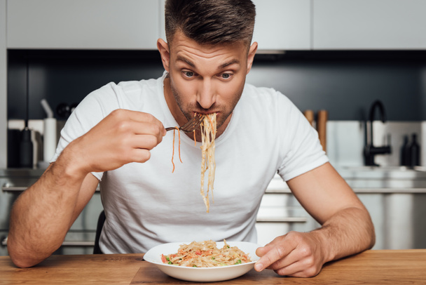 Man eating delicious noodles while sitting at kitchen table  - Photo, Image