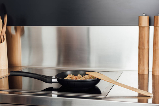 Espátula cerca de sartén con fideos en la estufa en la cocina
 - Foto, Imagen
