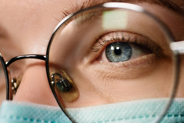 Μακροσκοπική άποψη του γιατρού με ιατρική μάσκα κοιτάζοντας μακριά φορώντας γυαλιά - Φωτογραφία, εικόνα
