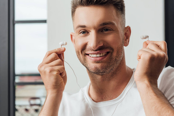 Handsome smiling man holding earphones at home  - Fotografie, Obrázek