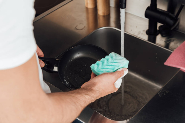 Gekropte weergave van de mens het reinigen van koekenpan met spons in de keuken  - Foto, afbeelding