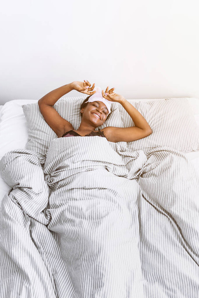 Usmívající se africká americká dívka ve spánkové masce probudil v ložnici - Fotografie, Obrázek