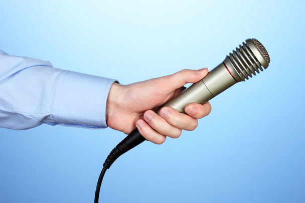 Male hand with microphone on blue background - Foto, afbeelding
