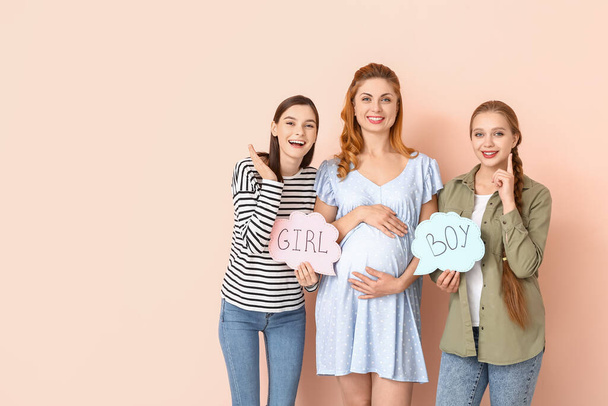 Coppia lesbica e donna incinta con parole scritte GIRL e BOY su carte sullo sfondo di colore. Concetto di maternità surrogata
 - Foto, immagini