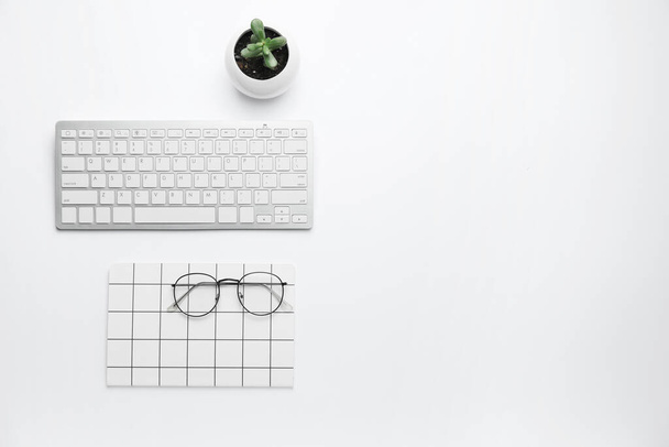 Πληκτρολόγιο υπολογιστή με σημειωματάριο και γυαλιά σε λευκό φόντο - Φωτογραφία, εικόνα