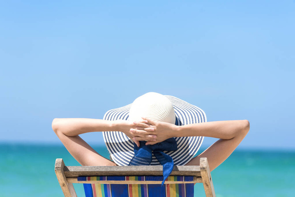 Літній час жінка відпочиває на пляжі. Весела жінка носить літню сукню і солом'яні капелюхи, які сидять на пляжі, дивляться на море. Час відпочити в літньому способі життя на відкритому повітрі на пляжі тропічного острова
. - Фото, зображення