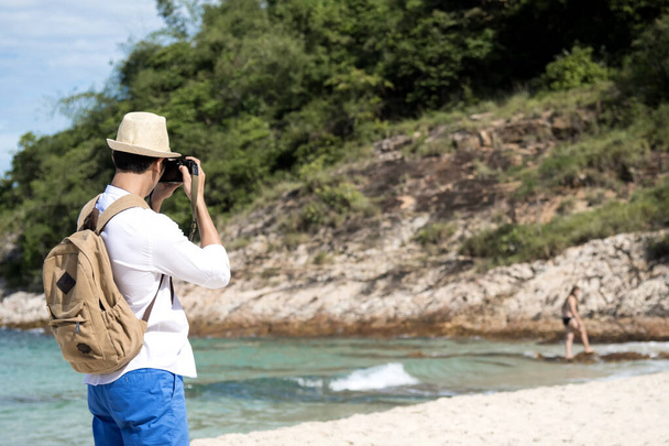Mladý muž cestovat venku na tropické pláži s modrým nebem a bílým mrakem pomocí profesionálního fotoaparátu DSLR vyfotit na dovolenou s láskou přírody. Venkovní cestovní životní styl koncept. - Fotografie, Obrázek