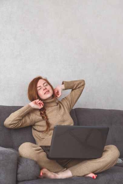 Mujer joven se está estirando después de terminar el trabajo o conferencia en línea en el sofá. Freelance, Trabajar en casa
 - Foto, Imagen