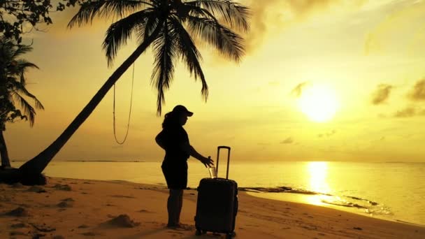 vrouw staand op tropisch strand met koffer bij zonsondergang - Video