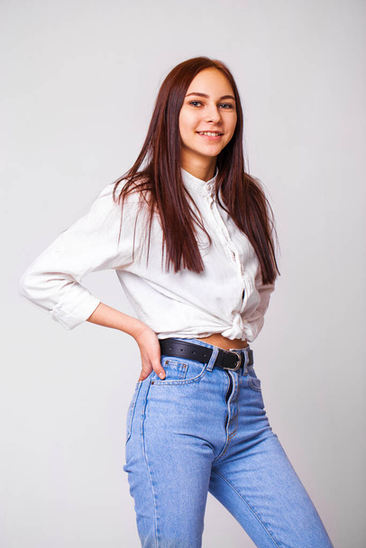 Closeup portrait of a young beautiful girl in blue jeans - isolated on gray background - Фото, зображення