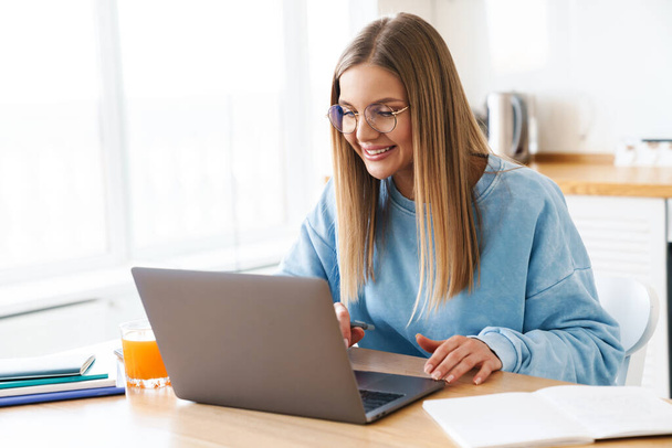 Obraz wesołej uroczej kobiety w okularach uśmiechniętej podczas pracy z laptopem w domu - Zdjęcie, obraz