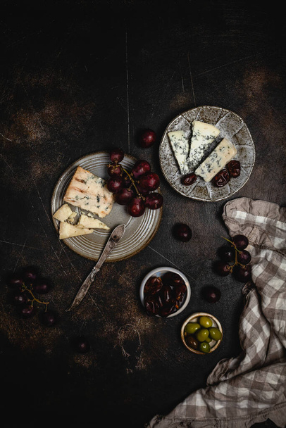 plates with blue cheese and red grape with dates and olives in bowl on dark background  - Foto, Bild