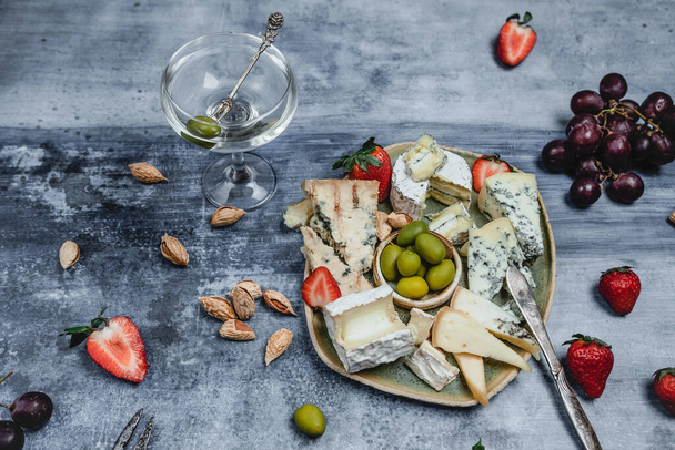 plate with set of cheese and strawberries and olives with martini glass on grunge background - Фото, зображення