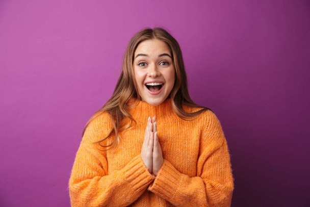 Image of happy young woman wearing sweater smiling and praying with palms together isolated over purple background - Фото, зображення