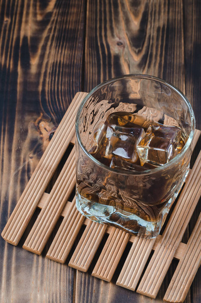 Glass of cognac with ice cubes on a wooden table/Glass of cognac with ice cubes on a wooden table. Top view. - Foto, Bild