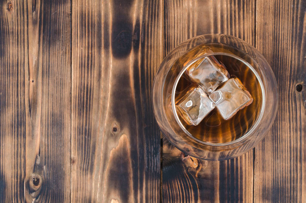 Glass of cognac with ice cubes on a wooden table/Glass of cognac with ice cubes on a wooden bar. Top view, copyspace - Valokuva, kuva
