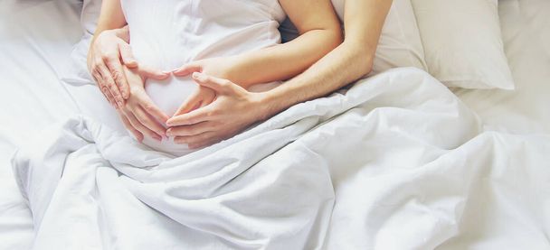 Беременная женщина с мужчиной, обнимающим живот в постели. Выборочный фокус. люди
. - Фото, изображение