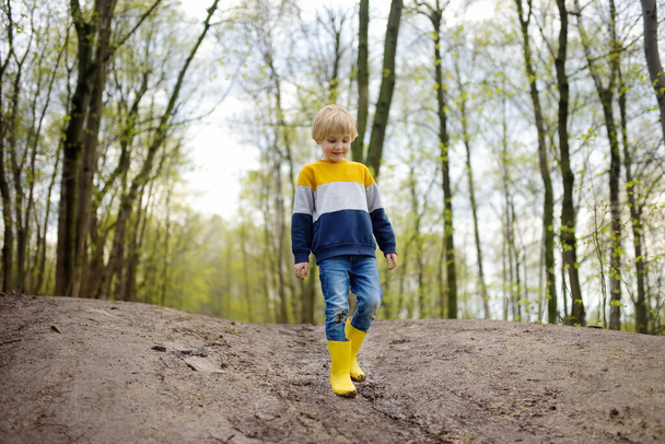 Mischievous preschooler child wearing yellow rain boots walking by muddy road. Kid playing and having fun. Outdoors games for children. - Фото, зображення